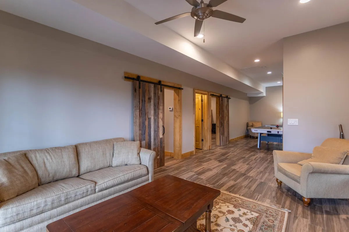 A welcoming game room featuring a comfortable sofa, a coffee table, and a pool table. Wooden sliding doors add a rustic touch and may suggest access to outdoor spaces or views beyond. The setup is ideal for family game nights, socializing, and relaxed gatherings after enjoying seasonal outdoor activities.