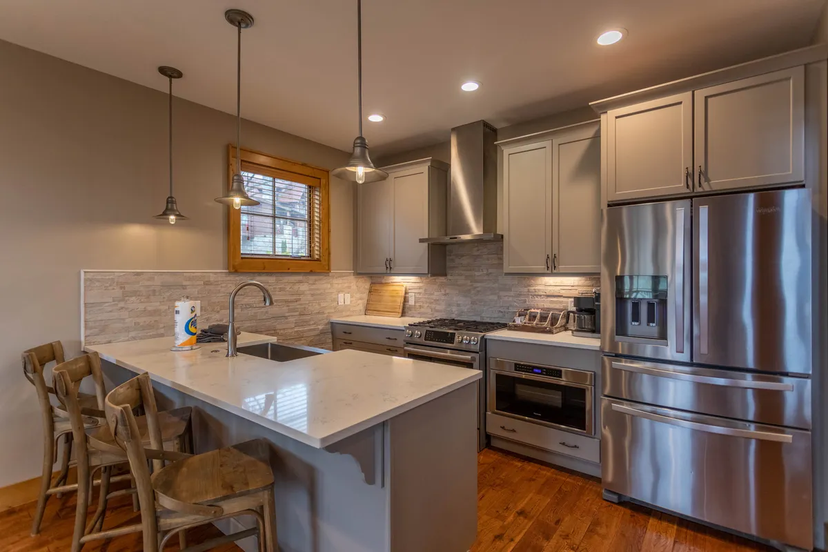 A close-up of the stylish kitchen island with quartz countertops, sleek stainless steel appliances, pendant lighting, and wooden stools. The kitchen looks inviting and functional, with ample space for meal prep and family interaction.