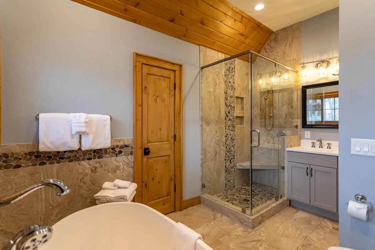 A serene, spa-inspired bathroom featuring a freestanding bathtub, glass walk-in shower, and natural wooden accents. The ambiance is tranquil and inviting, evoking resort-style relaxation.
