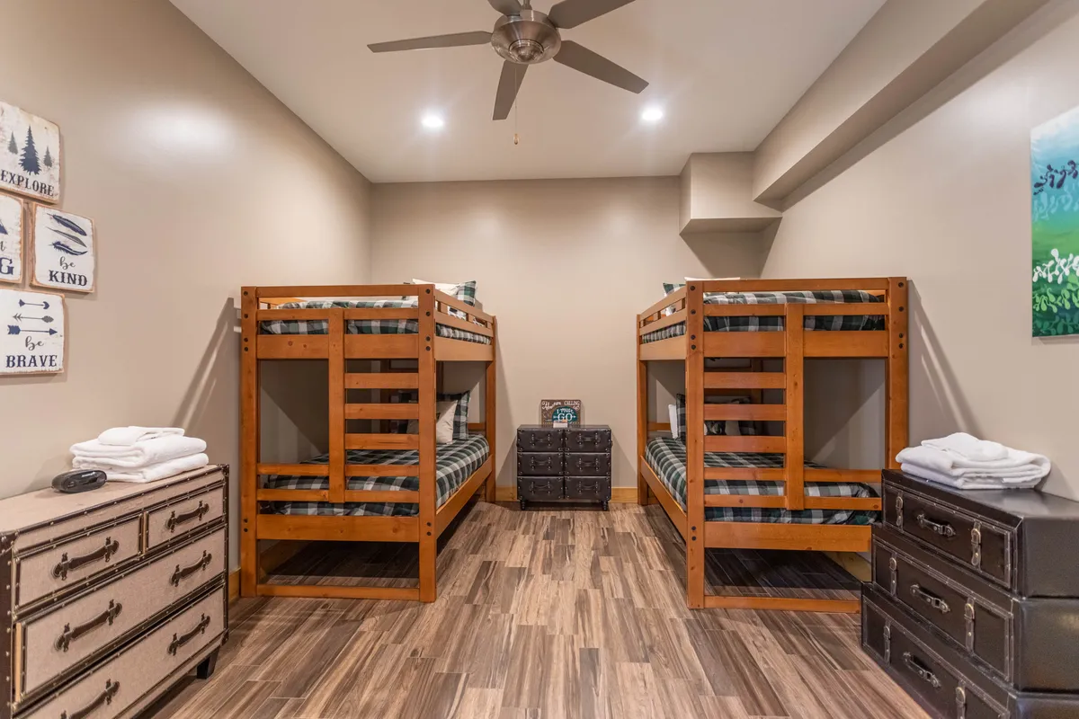 A bright and playful bunk room with two twin-over-twin bunk beds, wooden storage chests, and cheerful artwork. The space feels welcoming and functional, tailored for kids and teens to sleep or play together.